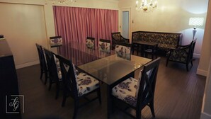 Een eetkamer met een glazen tafel omringd door stoelen met bloemenmotieven, een kroonluchter en een bank met een bloemenprint.