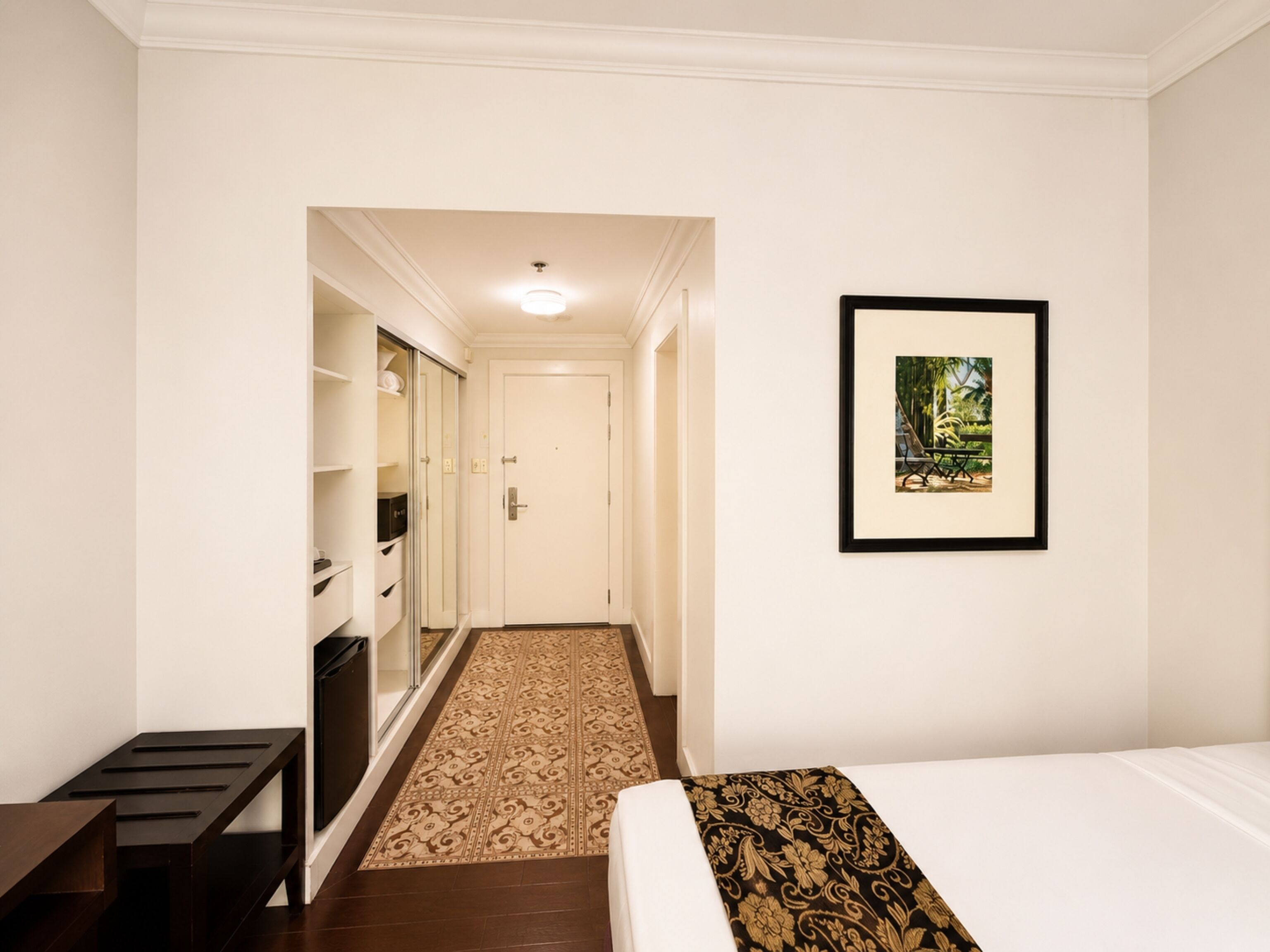 A hotel room with a bed, a framed picture on the wall, a wardrobe, and a small table.