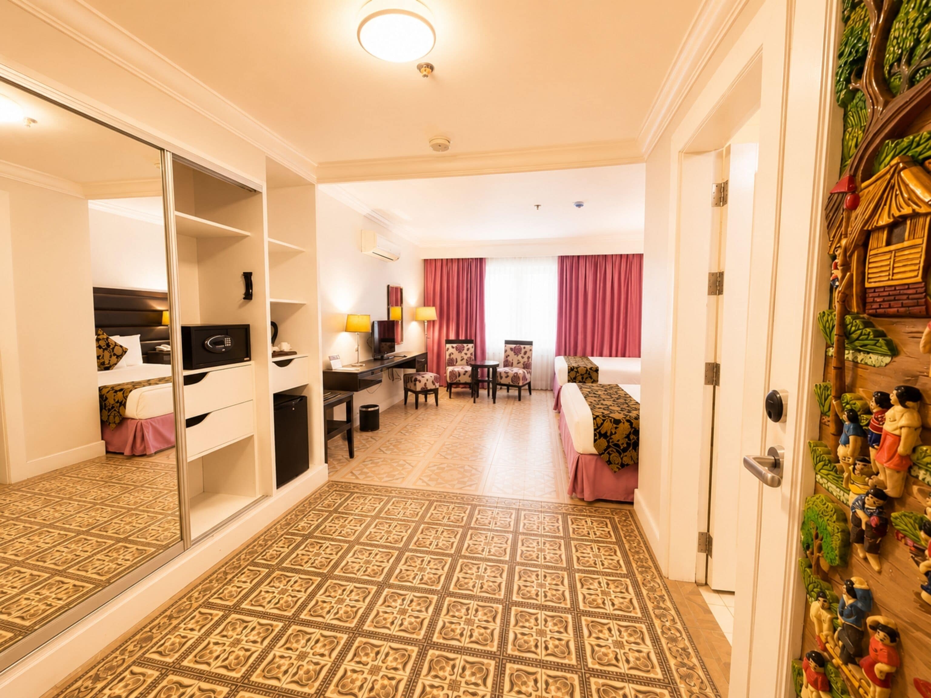 A hotel room with a mirrored closet, a desk with a computer, a dining area with chairs, a bed, and a decorative wall.