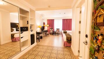 A hotel room with a mirrored closet, a desk with a computer, a dining area with chairs, a bed, and a decorative wall.