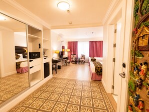 A hotel room with a mirrored closet, a desk with a computer, a dining area with chairs, a bed, and a decorative wall. - Fiesta Garden Hotel (Bantay)