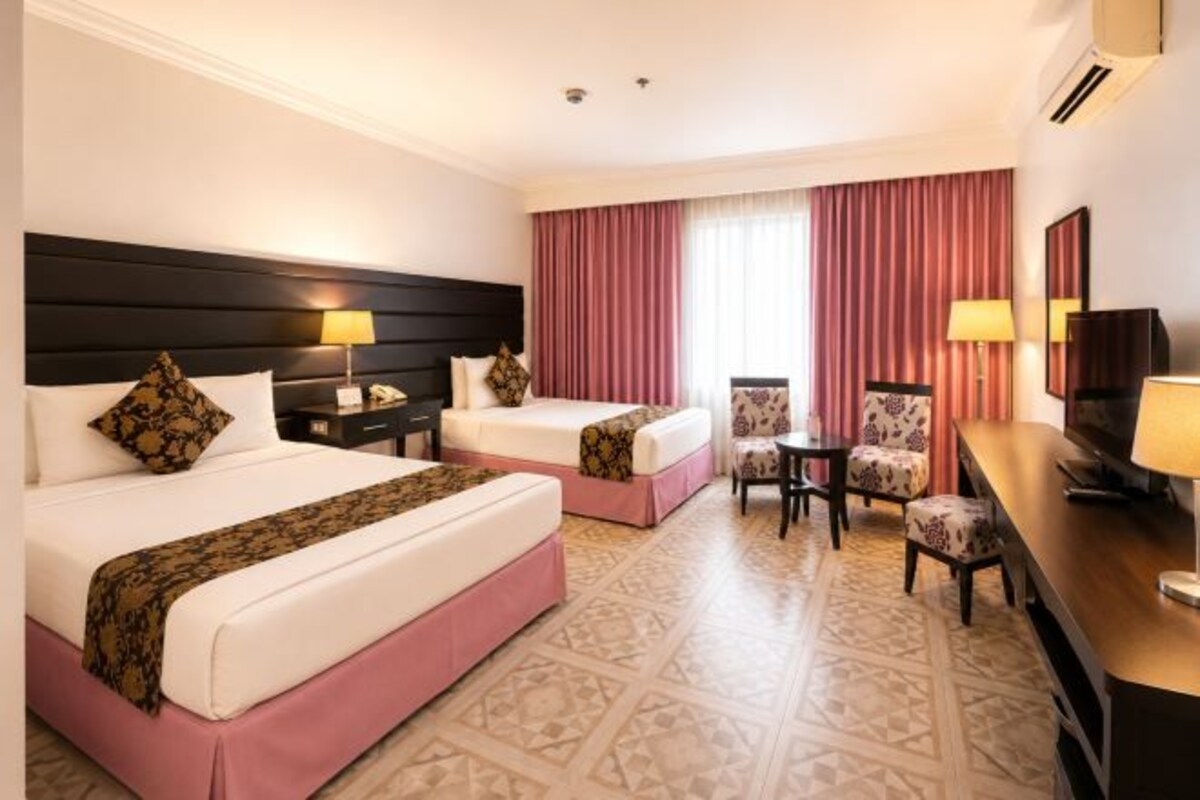 A hotel room with two beds, a desk, a chair, and a TV.