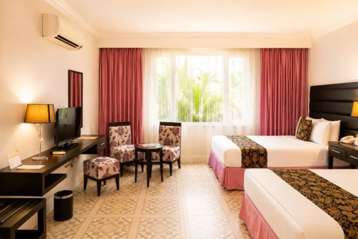 A hotel room with a bed, a desk with a computer, a chair, a TV, and a window with curtains.