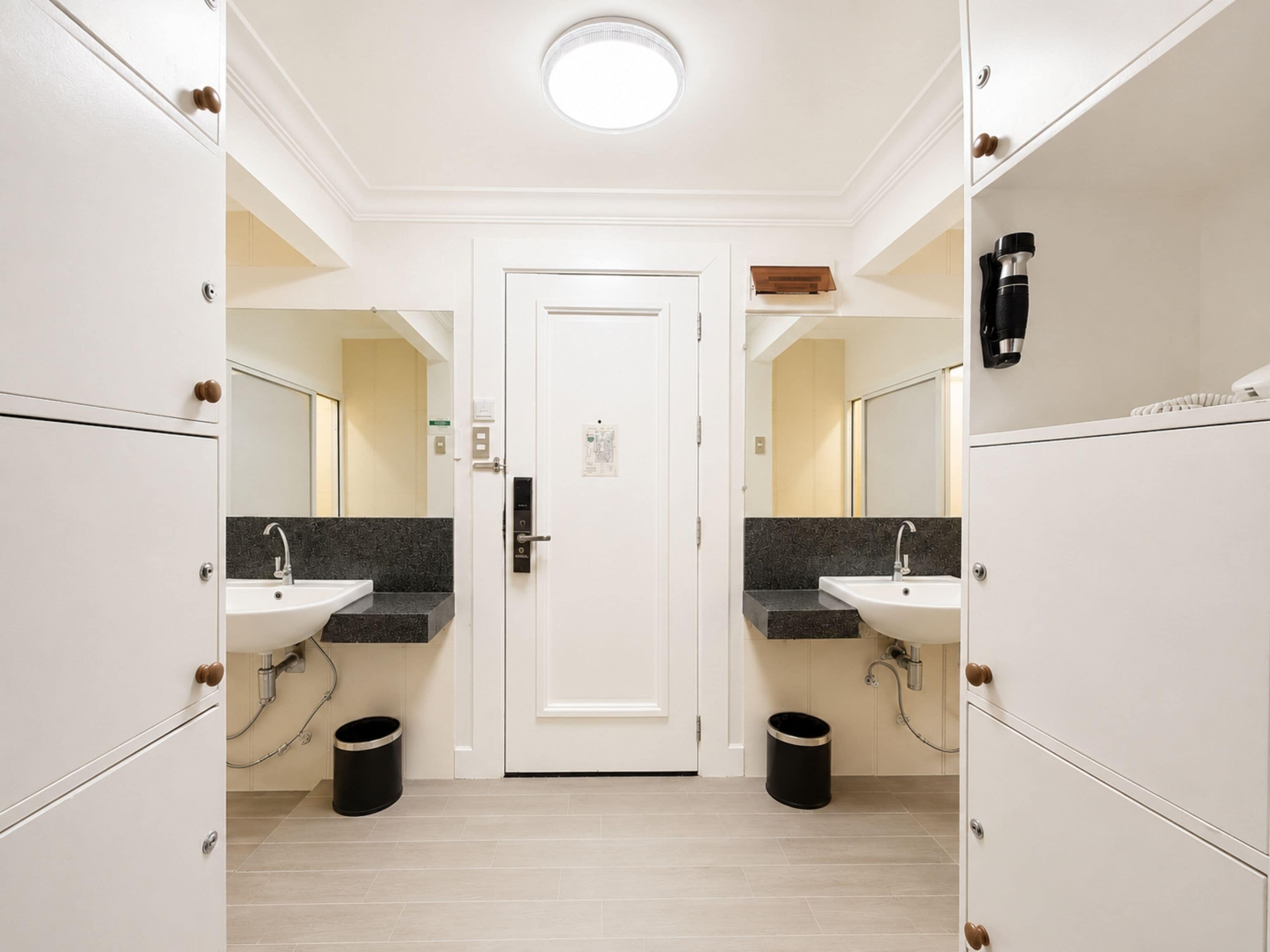 Een moderne badkamer met twee wasbakken, een witte deur en een plafondlamp.