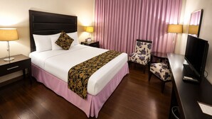 A hotel room with a bed, bedside tables, a chair, a desk with a television, and a large window with curtains. - Fiesta Garden Hotel (Bantay)