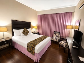 A hotel room with a bed, bedside tables, a chair, a desk with a television, and a large window with curtains. - Fiesta Garden Hotel (Bantay)