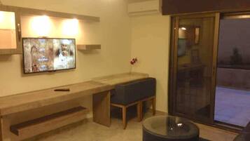 A living room with a TV, a bench, a glass coffee table, and a sliding glass door.
