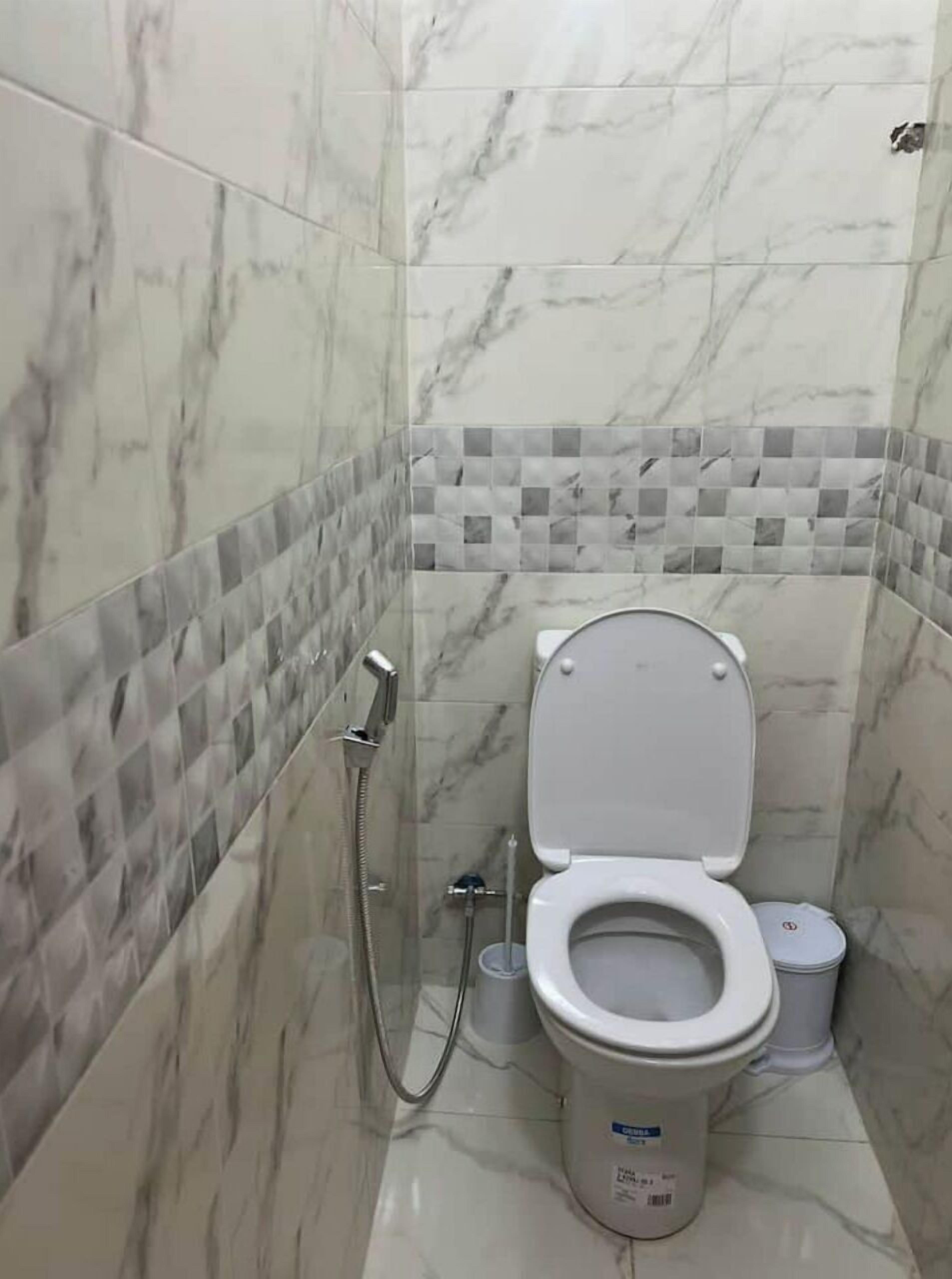 Kylpyhuone, jossa on wc, suihku ja laatoitettu seinä.