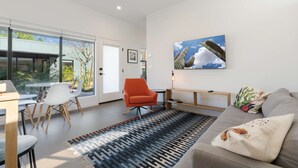 Ein modernes Wohnzimmer mit großem Fenster, einem roten Sessel, einem grauen Sofa und einem gemusterten Teppich.