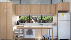 A modern kitchen with wooden cabinets, a large window, a white refrigerator, and a small island with stools. - Eco-friendly 2-bedroom Container - 80 Walkscore! (Phoenix)