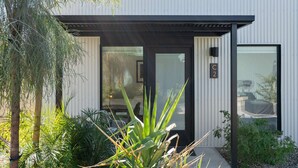 A modern building with a black-framed entrance, a glass door, and a small garden area with plants and a bench. - Eco-friendly 2-bedroom Container - 80 Walkscore! (Phoenix)