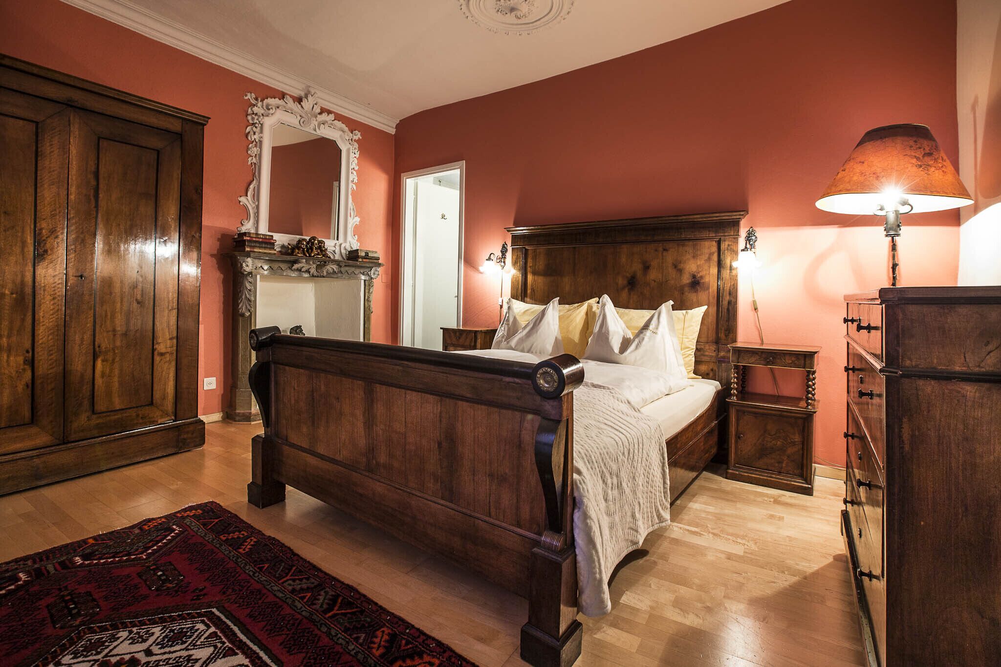 Un dormitorio tradicional con una cama de madera, un espejo grande y una alfombra roja.