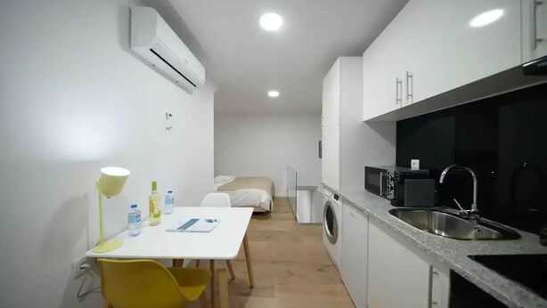 A compact kitchen with a sink, microwave, and a washing machine. There is a small dining area with a table and chairs.