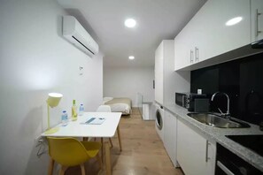 Une cuisine compacte équipée d’un évier, d’un four à micro-ondes et d’un lave-linge. Un petit coin repas avec une table et des chaises est également disponible.