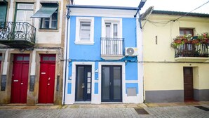A two-story building with a blue facade, red doors, and a balcony with potted plants.