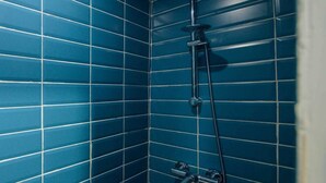 A bathroom with blue tiled walls and a shower with a handheld showerhead and a handheld faucet.