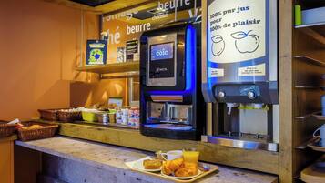 Una estación de café con una máquina de café digital, una selección de pasteles y un cartel que indica que el café está hecho con ingredientes franceses 100%.
