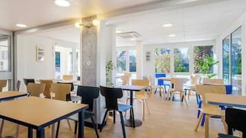 Un espace intérieur spacieux, doté de nombreuses tables et chaises, de grandes fenêtres laissant entrer la lumière naturelle et offrant une vue sur la verdure environnante.