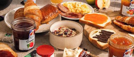 A breakfast table with croissants, ham, eggs, and various jams.