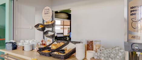 A breakfast buffet with baskets of croissants, plates, cups, and a coffee machine.