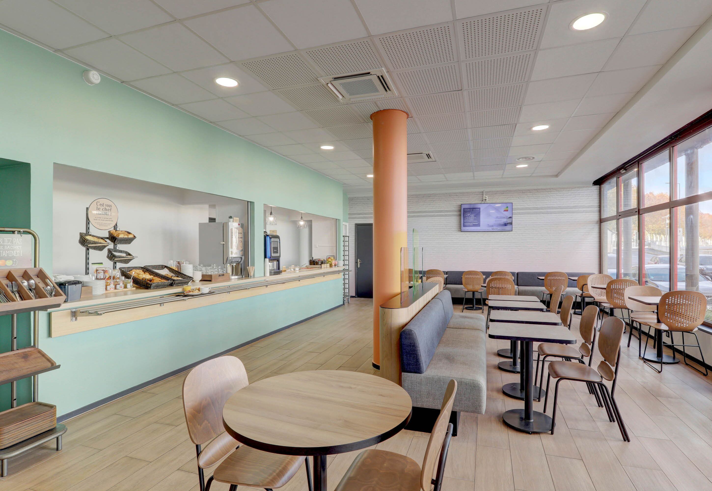 Una cafetería moderna con mostrador, zona de estar y grandes ventanales.