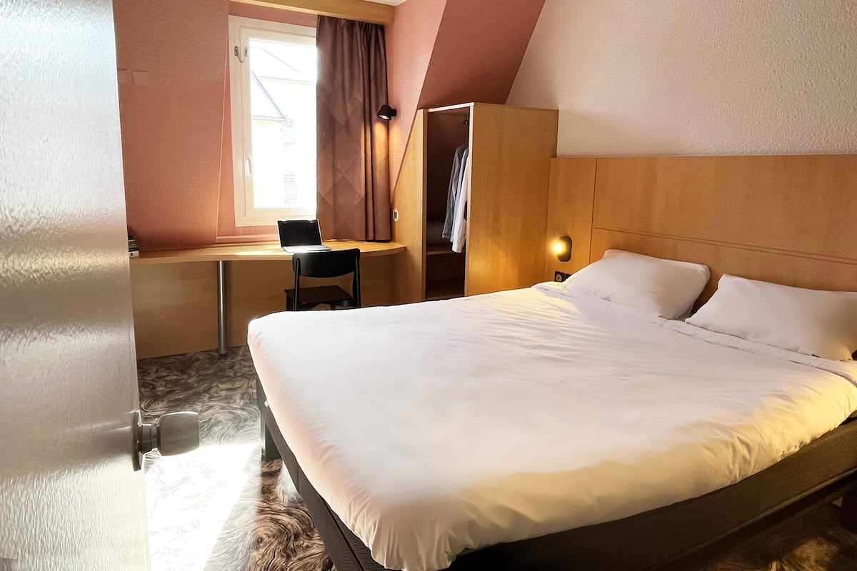 A hotel room with a bed, a desk, a chair, and a wardrobe.