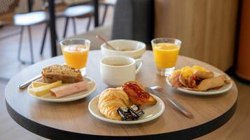 A breakfast setting with croissants, ham, cheese, toast, and orange juice on a table.