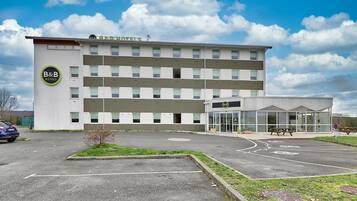 A B&B hotel with a modern design, multiple floors, and a parking area with marked spaces.