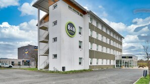 Un hôtel de type « bed and breakfast » au design moderne, avec un logo bien visible, plusieurs balcons et un espace de stationnement.