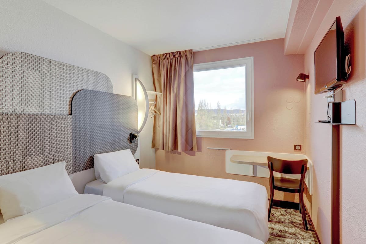 Habitación de hotel con dos camas, un escritorio, una silla, un televisor y una ventana con vistas.