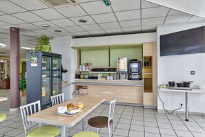 Een moderne cafeteria met een balie, zithoek en een koelkast met een plant erop.