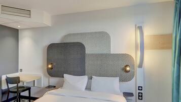 Une chambre d’hôtel avec un lit, un bureau et une chaise. La tête de lit présente un motif texturé et deux lampes sont fixées au mur.