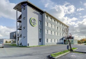 A modern B&B hotel with a curved facade, multiple balconies, and a parking area.