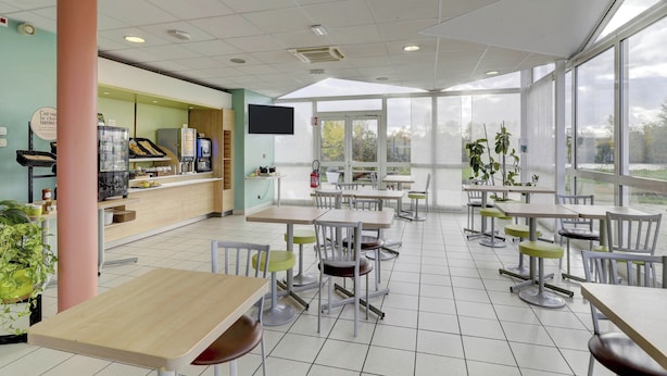 Un espace intérieur spacieux, doté de nombreuses tables et chaises, de grandes fenêtres et d’un comptoir avec un téléviseur.