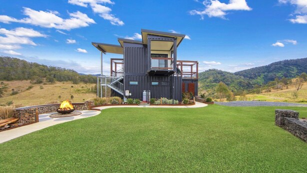 A modern house with a large deck, a fire pit, and a stone wall. - Bindera Container House (BINDERA)