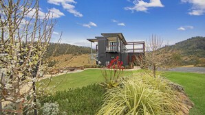 A modern two-story house with a balcony, surrounded by a well-maintained lawn and flowering plants. - Bindera Container House (BINDERA)