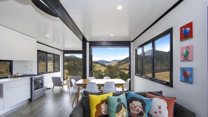 A modern kitchen with large windows, a dining area with a view of the countryside, and colorful artwork on the walls. - Bindera Container House (BINDERA)