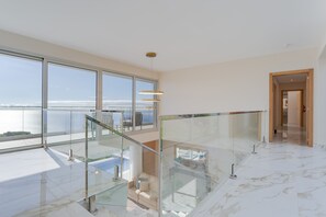 A spacious room with large windows, a glass railing, and a view of the sea.