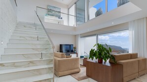 A modern living room with a marble staircase, a sofa set, a wooden coffee table, and a large window with a city view. - Villa Dia Dourado - Luxury villa on Madeira's south coast. (Ponta do Sol)