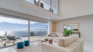 A modern living room with a large glass window offering a view of the sea. - Villa Dia Dourado - Luxury villa on Madeira's south coast. (Ponta do Sol)