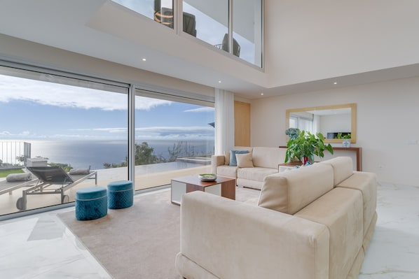 A modern living room with a large glass window offering a view of the sea.