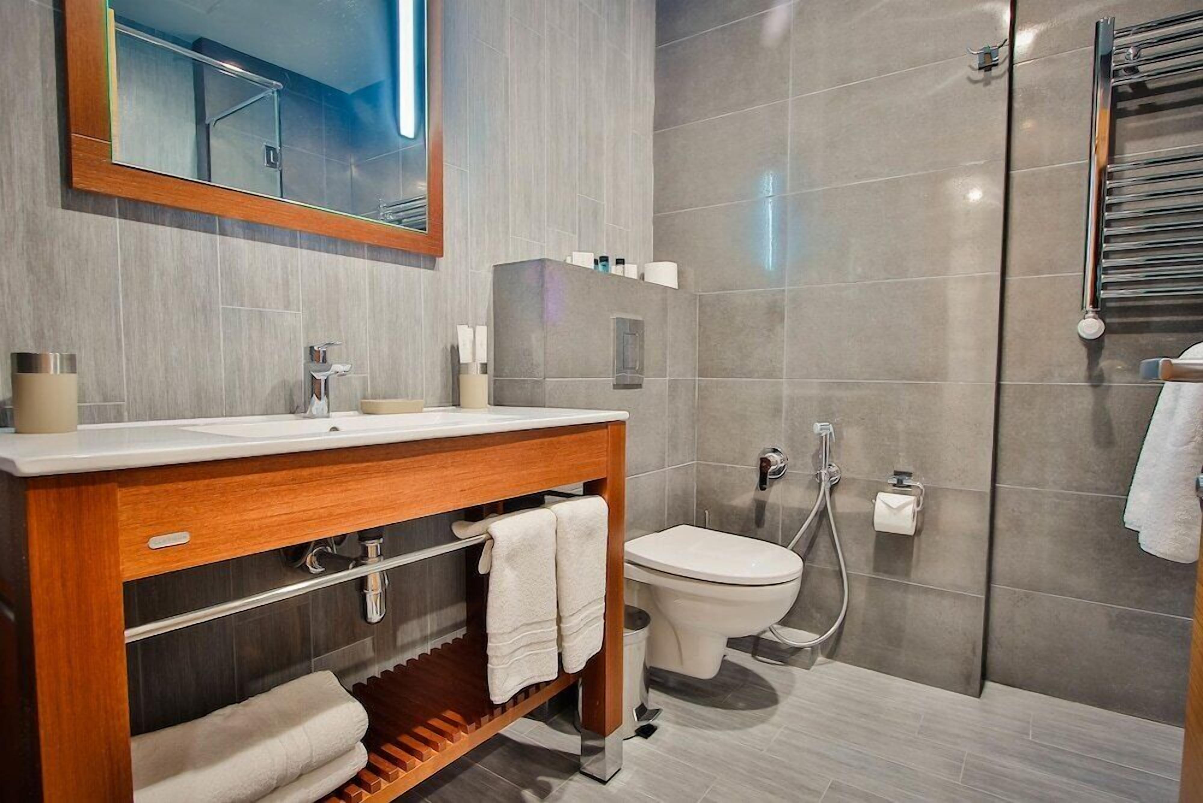 A modern bathroom with a wooden vanity, a toilet, a shower, and a large mirror.
