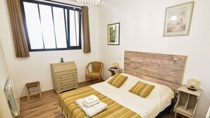 A bedroom with a large bed, a dresser, a chair, a nightstand, and a window with curtains.