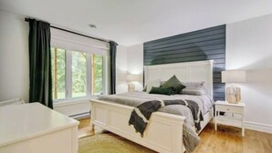 A bedroom with a bed, bedside tables, a window with curtains, and a view of greenery outside.
