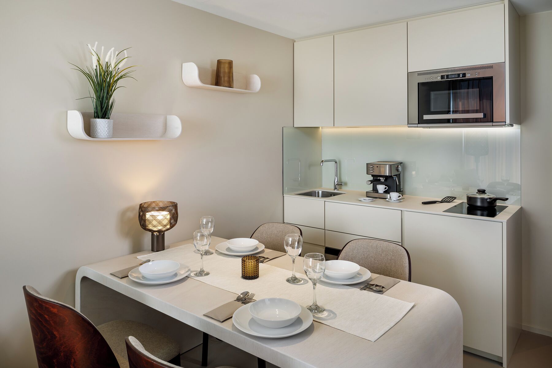 A modern kitchen with a built-in oven, a coffee machine, and a dining area with a table set for four.