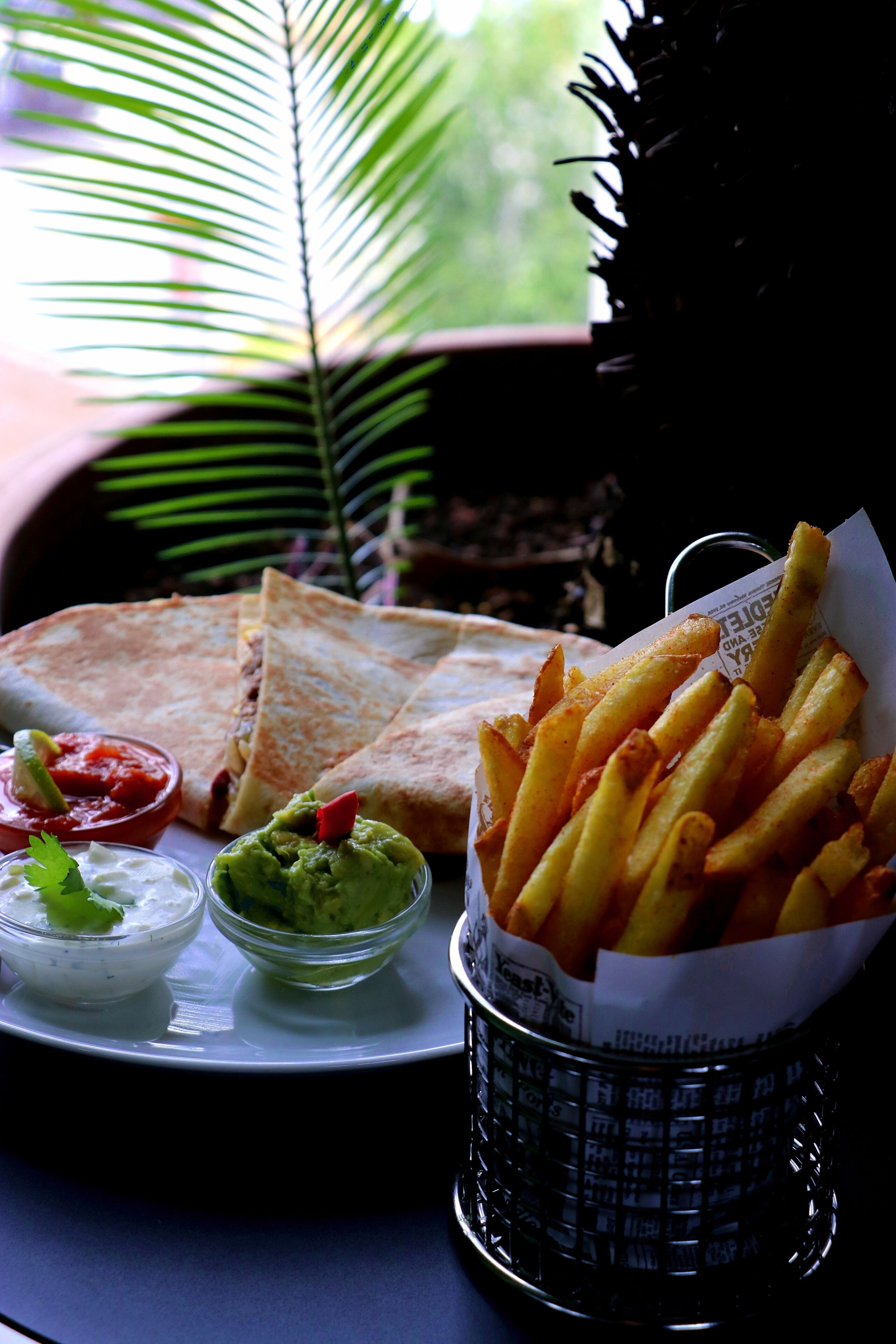 Un plato con quesadillas, papas fritas y dos recipientes pequeños de salsas.
