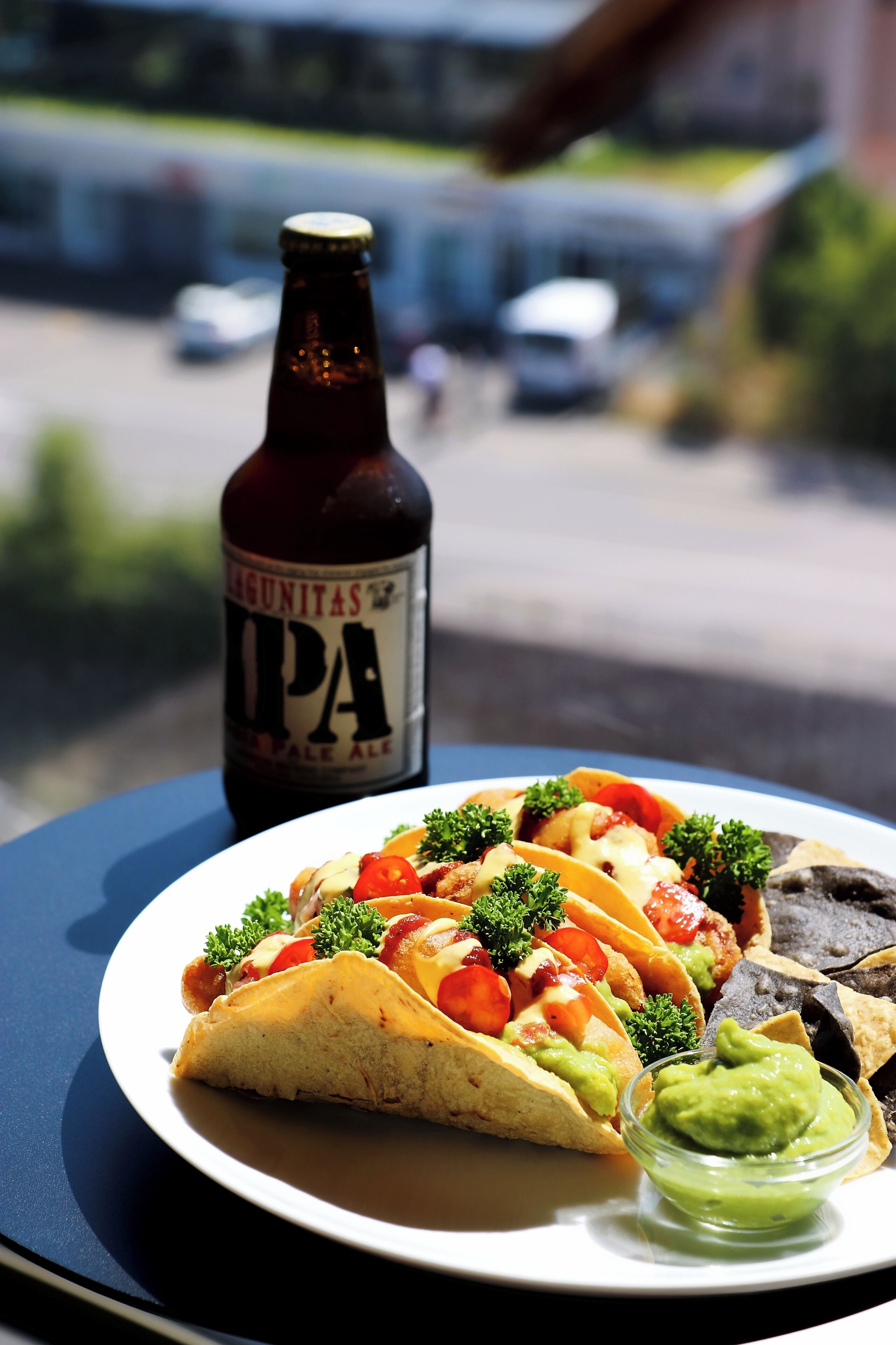 Een bord met taco's, guacamole en een fles Lagunitas IPA bier op een tafel.