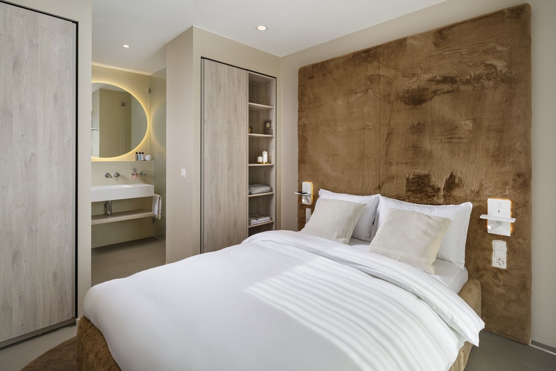 A bedroom with a bed, a large mirror, a wardrobe, and a built-in shelf unit.