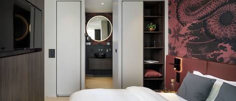 A bedroom with a bed, a mirror, a wardrobe, a bathroom with a sink, and a decorative wall.