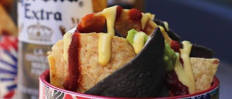 A colorful bowl with nachos and a bottle of Corona Extra beer in the background.